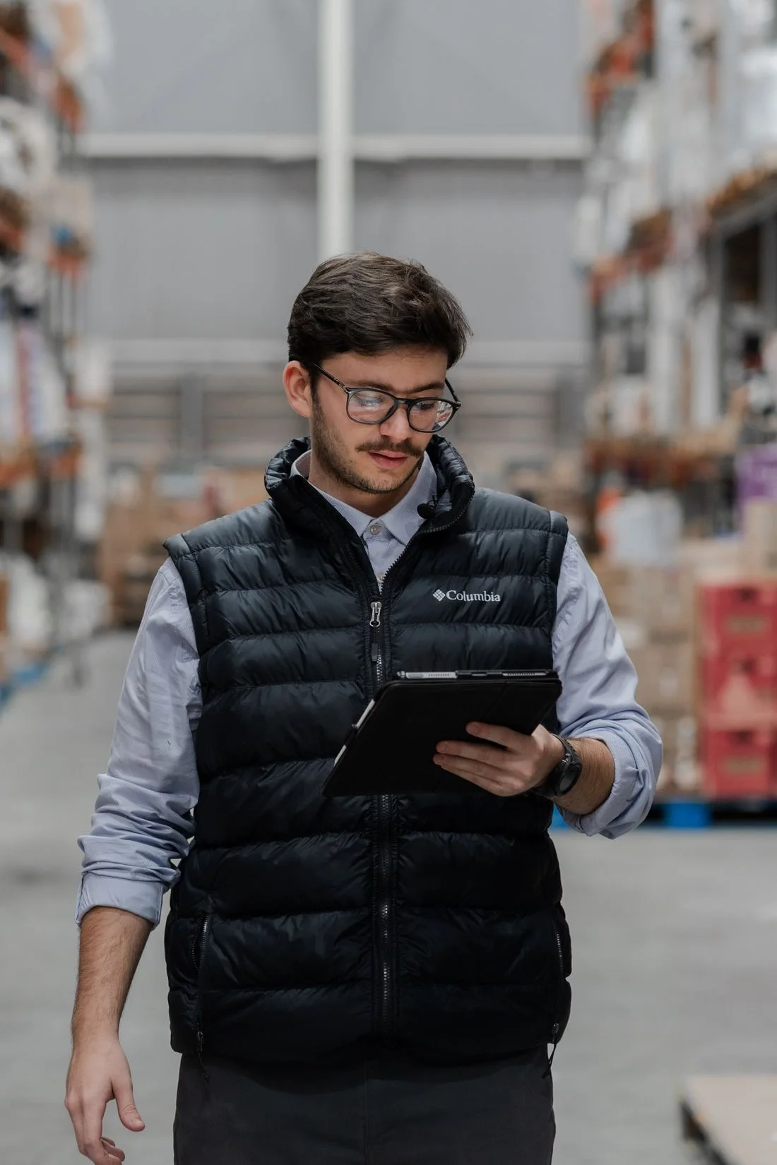 A warehouse worker checking inventory on a tablet between stocked shelves.